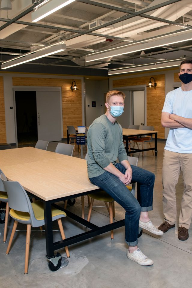 Two entrepreneurs in masks show off their workspace
