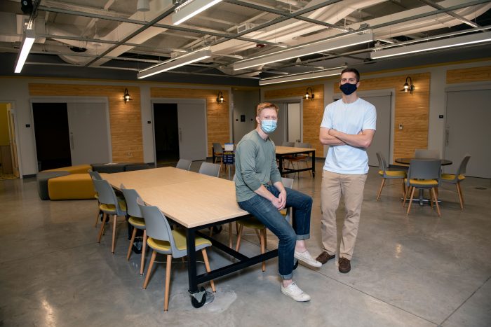 Two entrepreneurs in masks show off their workspace