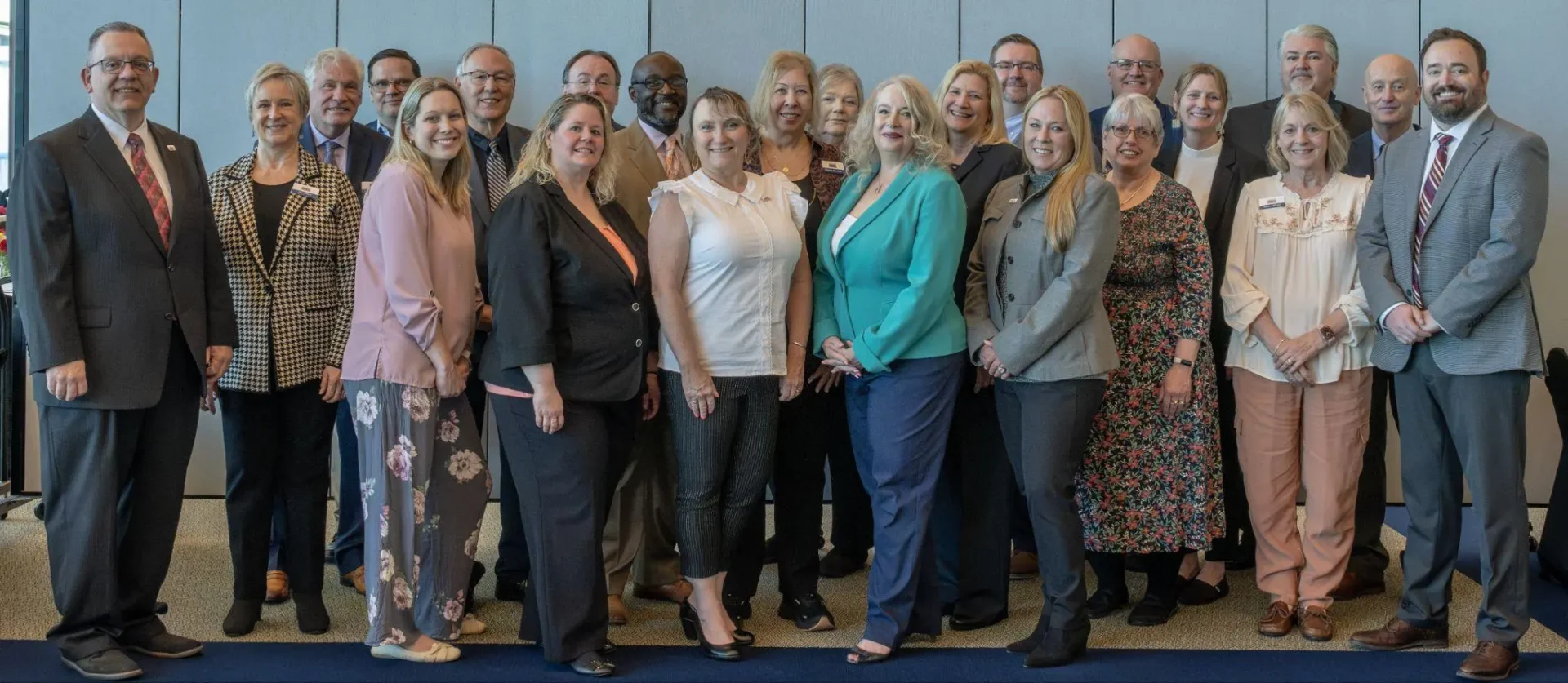 A group of people is standing together, posing for a group photo in a professional setting. They are dressed in business attire and appear to be attending an event or meeting.